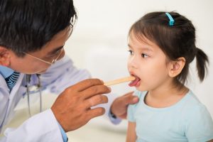 A child's mouth is wide open with tonsils enlarged, visible in the white or yellowish tinge