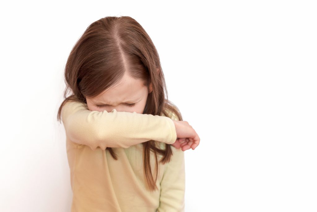 Young girl coughs or sneezes into elbow to protect others from contagious tonsillitis Young girl coughs or sneezes into elbow to protect others from contagious tonsillitis