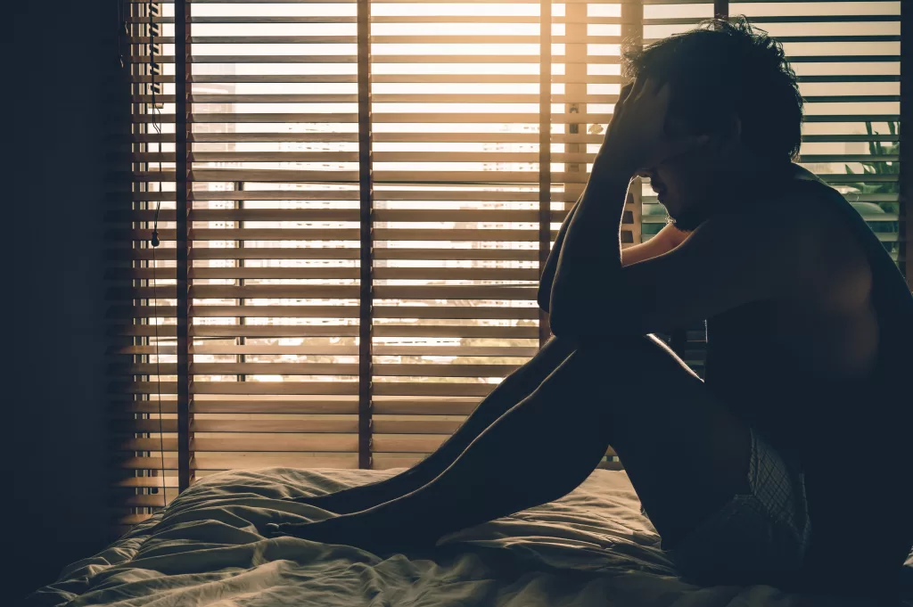 Depressed man sitting head in hands on the bed in a dark bedroom with low light environment Depressed man sitting head in hands on the bed in a dark bedroom with low light environment