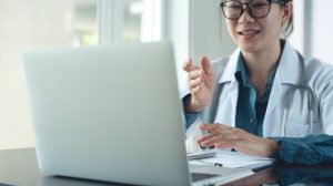 Sick girl wrapped in scarf holding tissue at face and consulting doctor online on video call