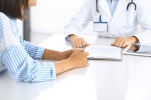 Young female doctor in white medical uniform with stethoscope using laptop for online consultation with a patient