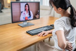 Asian,Woman,Worker,Patient,Consult,With,Doctor,For,Medical,Healthcare. Sick girl wrapped in scarf holding tissue at face and consulting doctor online on video call
