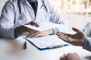 Asian,Male,Doctor,Talking,In,Clinic,Room,And,Handing,A Sick girl wrapped in scarf holding tissue at face and consulting doctor online on video call